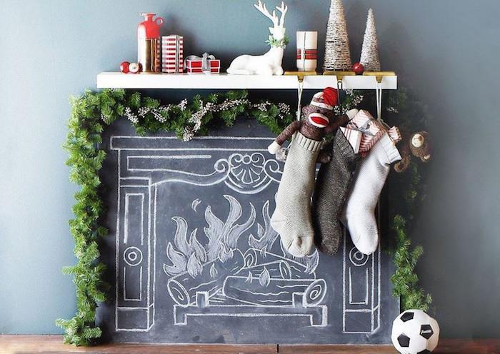 skalūnas su židinio imitacija, piešiamas kreida ant sienos kaip dekoratyvinė dirbtinė ugnis su kalėdine girlianda ir dekoratyviniais daiktais, kabančiais kojines