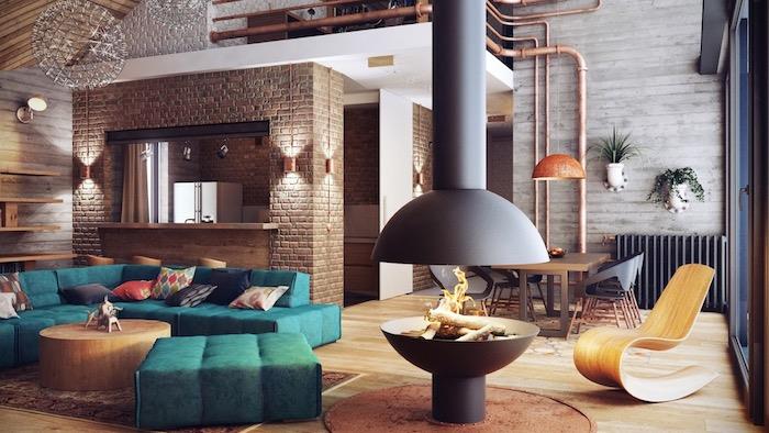 industrijski model dnevne sobe z račjim modrim kavčem in blatniki, okrogla lesena mizica za kavo, dizajnerski kamin, opečna stena za ločevanje kuhinje, lesen ležalnik, svetel parket