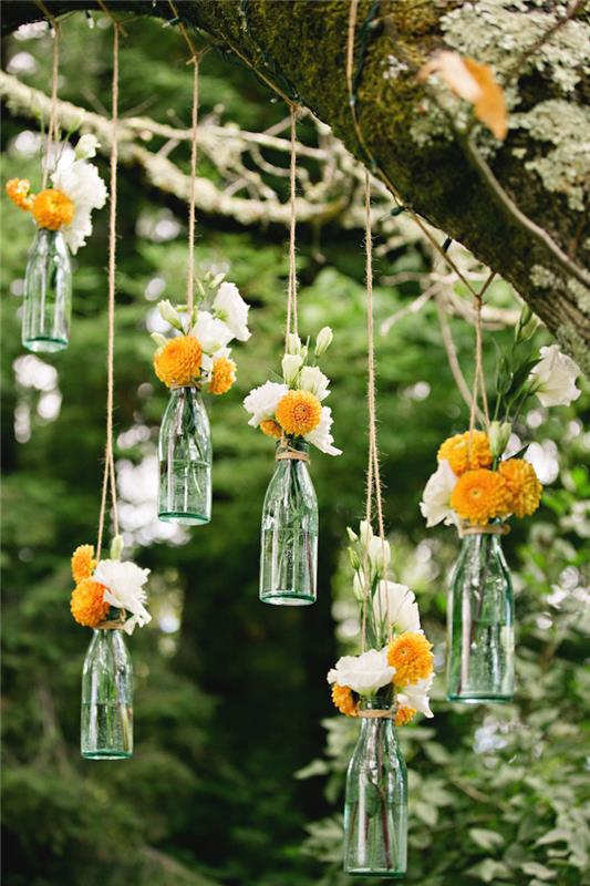 primer poceni poročne dekoracije, steklenice z oranžnimi in belimi cvetovi, majhne vaze, obešene z vrvicami z drevesne veje