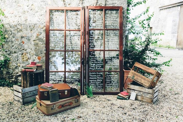 kmečki starinski poročni dekor z lesenimi in steklenimi vrati ter seznami gostov, ki so zapisani na ploščicah, starinskih deblih in lesenih zabojih, zelenih rastlinah
