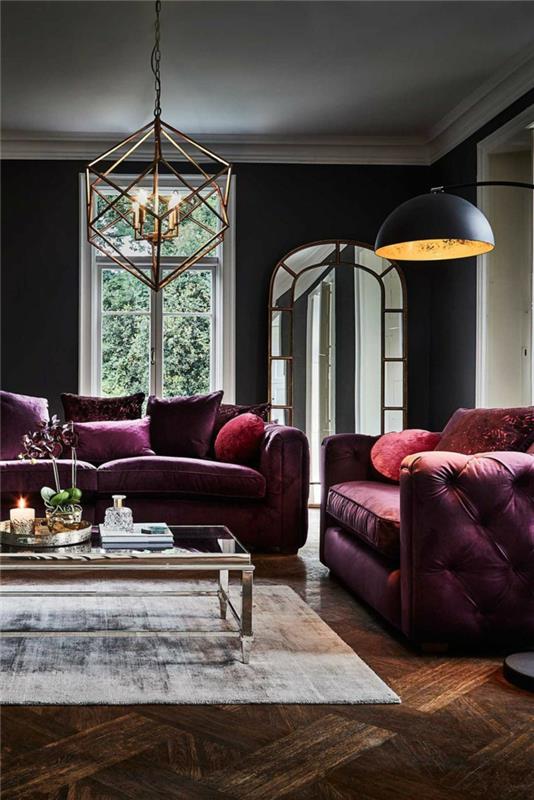 kokon dnevna soba v sivi in ​​vijolični barvi, steklena in zlata kovinska mizica, velike vijolične zofe, tovarniška viseča svetilka, geometrijska stropna svetilka