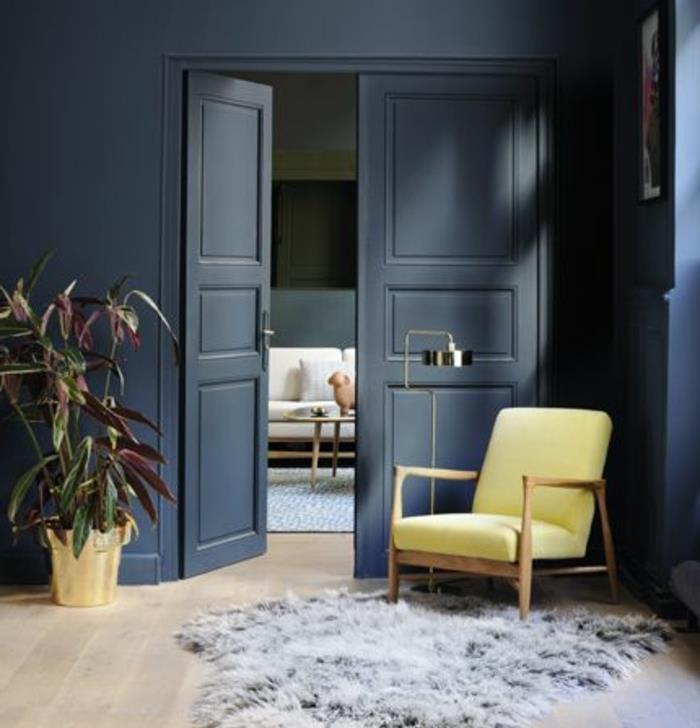 İskandinav oturma odası dekoru, gri mavi duvar, ahşap sandalye, sarı minder, gri kürklü halı, hafif parke, bitki