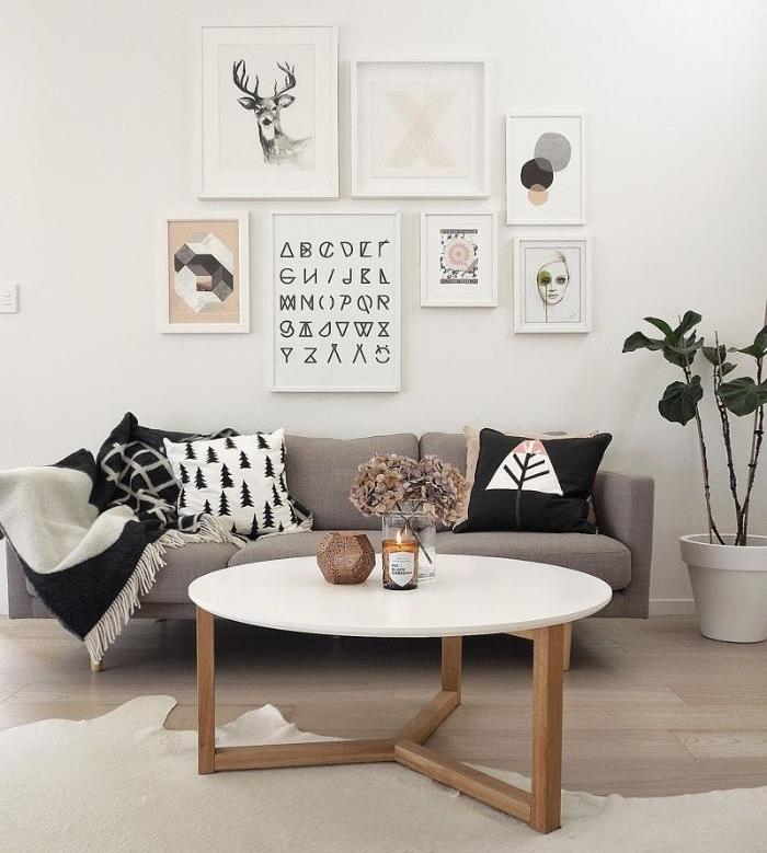 originali sienų apdaila abstrakčiuose grafikos paveiksluose šiltoje svetainėje su balta medine kavos staliuko pilka sofa, papuošta šviesaus medžio parketo pagalvėmis
