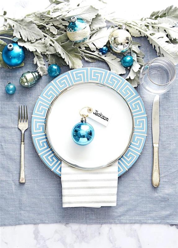 mavi Noel topunda yer tutuculu mavi ve beyaz tabak ve yeşillik ve mavi topların ortasında, bir Noel masası nasıl kurulur
