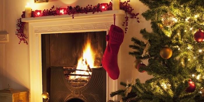 Manto üzerinde kırmızı meyveler ve gövdeler ile Noel şöminesi dekorasyonu ve yanda gerçek bir Noel ağacı