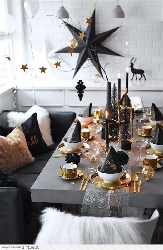 siva miza z zlato -belim jedilnim priborom in krožniki, svečami in črnimi dekorji ,, velika stenska dekoracija s črno zvezdo, elegantna novoletna dekoracija