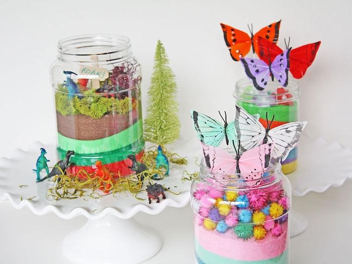 Renkli kum renkli ponponlar, yapay bitki örtüsü ve kağıt kelebekler ile bir cam kavanozda kendinizi şımartmak için kendin yap teraryum