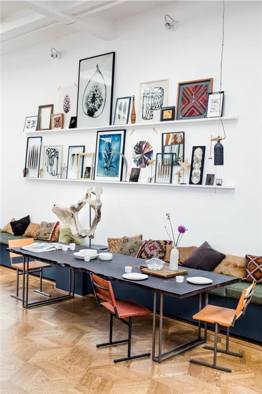 baltos sieninės lentynos, ilgas medinis stalas, minimalistinės kėdės, keli įrėminti paveikslai