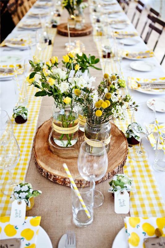 geltonai ir baltai languotas stalo bėgikas, mediniai rąstai, stiklo vazos, lauko gėlių puokštės