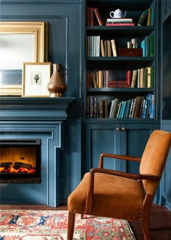 anties mėlynos spalvos svetainės dekoras, mėlyna knygų spinta su sieniniu židiniu, ochros spalvos fotelis