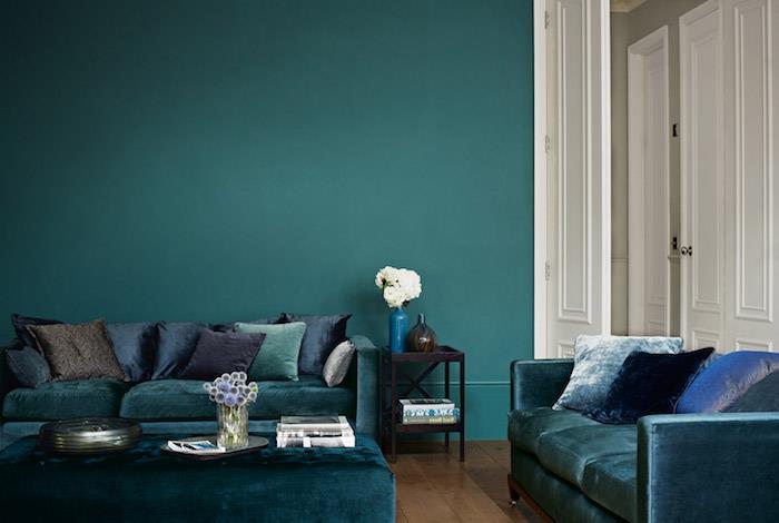 temno modra dekoracija dnevne sobe, ki se vleče v barvo nafte, rjavi parket, zofe in mizica v naftni senci, modre, zelene in temno sive blazine