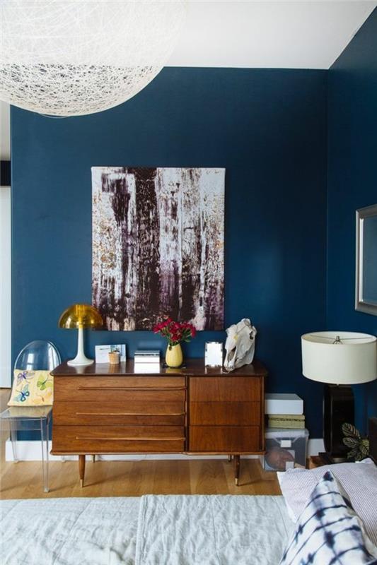 anties mėlynos spalvos svetainės dekoras, senovinė medinė komoda, toršeras ir maža akrilo kėdė