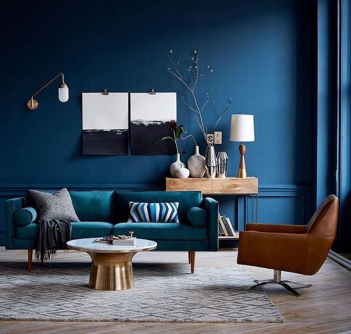 modra dekoracija dnevne sobe s pavno modrim kavčem in rjavim usnjenim naslonjačem, sivo -bela preproga, medeninasta miza, stene s črno -belo umetnostjo