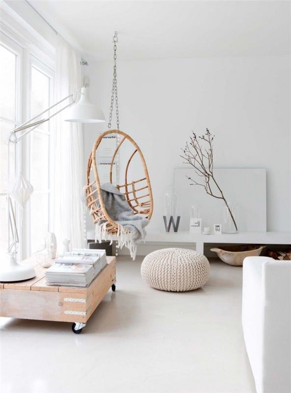 baltas interjeras švariame skandinaviško stiliaus gyvenamajame kambaryje su vidinėmis sūpynėmis iš rotango ir megztu pufu