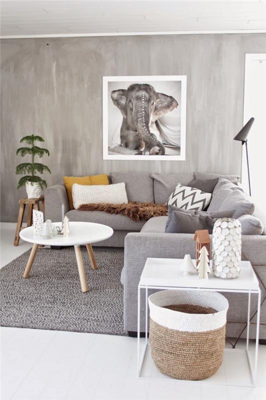 pilkas modernaus skandinaviško stiliaus svetainės dekoras su didele pilka kampine sofa, padengta vientisos spalvos dekoratyvinėmis pagalvėmis arba geometriniais raštais ir dekoratyviniais natūralios medienos akcentais, pilkos sienos cemento efektu, sustiprintu dideliu nuotraukų plakatu