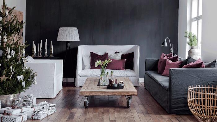 siva dekoracija dnevne sobe, ogljeno siva naglasna stena, siv kavč, beli naslanjači, lesena tla, lesena mizica s kolesi, božično drevo