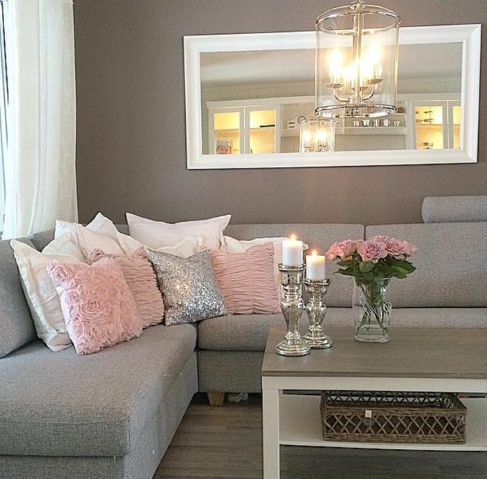 siva dekoracija dnevne sobe, roza in bele blazine, srebrni svečniki, veliko pravokotno ogledalo