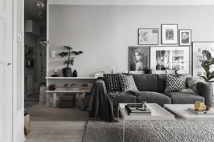 sivo -beli dekor dnevne sobe ogljen siv kavč, pletena siva preproga, bele mizice, lesena tla, stenska dekoracija črno -belih fotografij
