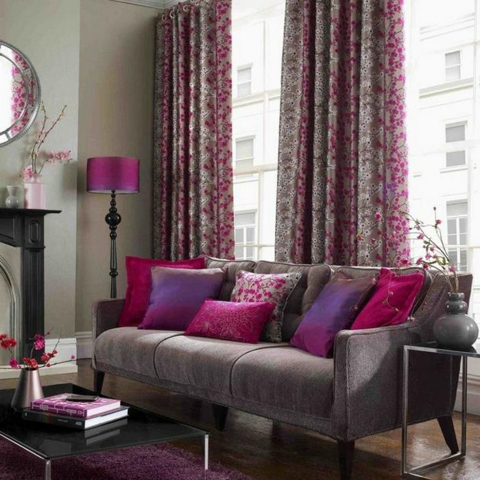 pilkas svetainės dekoras, šviesiai pilka sofa, alyvinės ir fuschijos pagalvėlės, aviečių ir pilkos spalvos užuolaidos, alyvinė šviestuvo lemputė