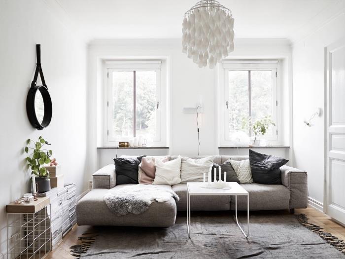 sivo -beli dekor dnevne sobe, siv kavč in preproga, blazine, siva, bela in roza, siva krzna, originalna viseča svetilka, kup knjig, majhno okroglo ogledalo