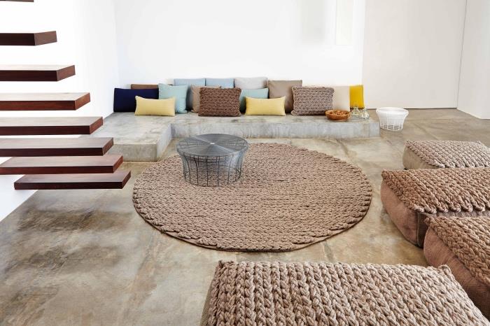 modern oturma odası dekor fikri, bej zemin ve beyaz duvar, etnik kahverengi halı ve koltuklar, yüzer merdiven, yerde beton kanepe, renkli minderler
