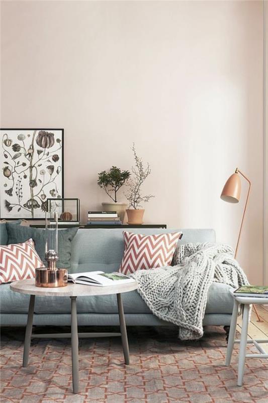 modernus svetainės dekoras, skandinaviškas mažas stalas, pilka sofa, varinė grindų lempa, pilkai megztas pledas, silkių rašto pagalvėlės