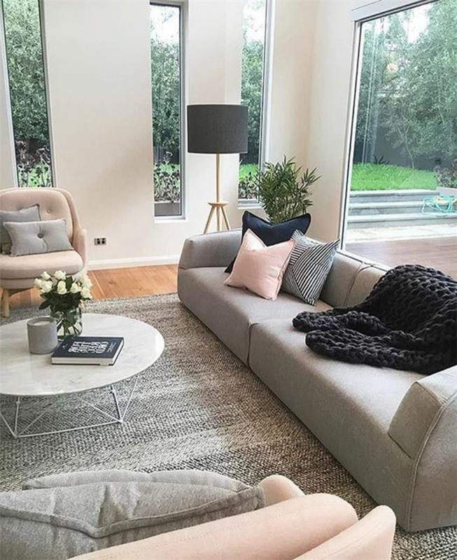 modernus svetainės dekoras, pilka sofa, rausvos ir pilkos spalvos dekoratyvinės pagalvėlės, skandinaviško stiliaus apvalus stalas, juodas megztas pledas
