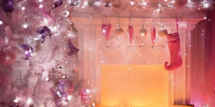 Beyaz bir ağaç ve şöminenin mantosundan sarkan ışıklar ile pembe Noel oturma odası dekoru