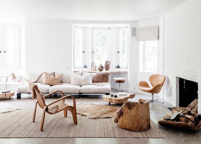 Skandinaviško minimalistinio stiliaus svetainės dekoras su žema sofa su šviesiai pilkomis pagalvėlėmis priglaudžia medines taburetes modernus baltas židinys baltos sienos