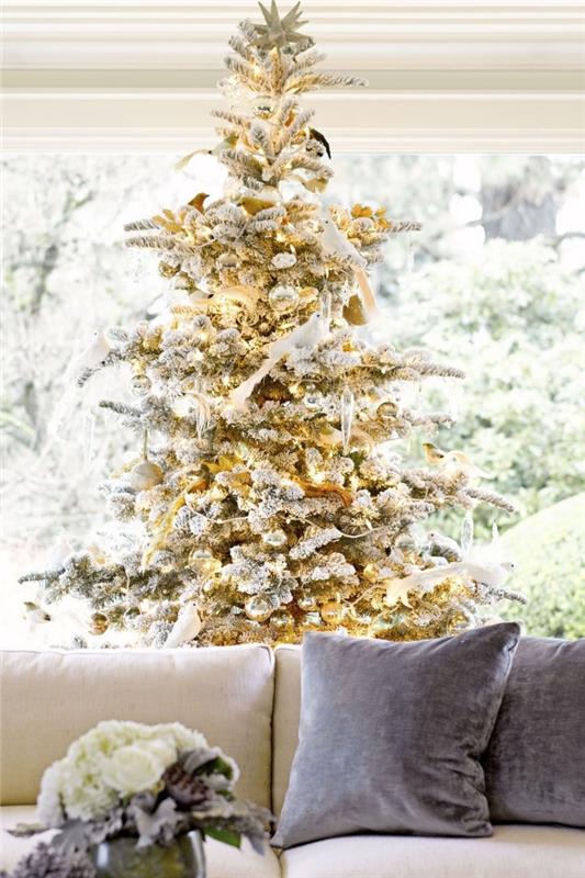 iç tasarım trendi yılbaşı 2019, bej kumaş kanepe ve altın ve gümüş Noel ağacı ile döşenmiş büyük pencereli oturma odası