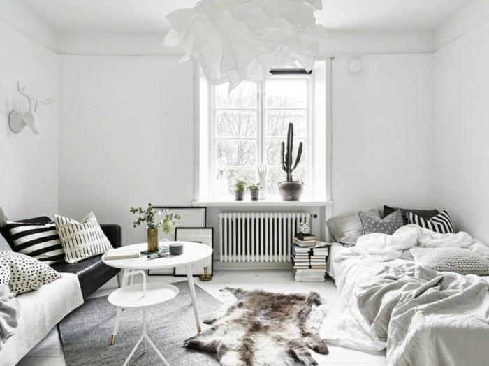 skandinaviška lova-žema-sofa-juodos pagalvėlės-įvairūs raštai-pilkai balti ir juodi-kai kurie augalai-baltos kavos staliukas ir pakaba-kuri imituoja baltą gėlę