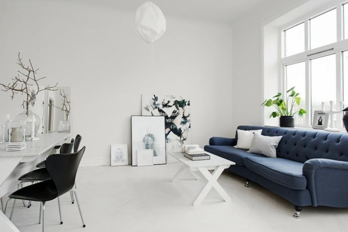 İskandinav dekor fikri, zıt koyu mavi kanepe, beyaz zemin ve duvar kaplaması, beyaz sehpa, grafik tasarım dekoru, İskandinav aksesuarları ile tamamen beyaz dekor