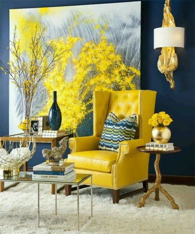 İskandinav oturma odası dekoru, sarı koltuk, beyaz kürk halı, sehpa, sarı ve gri soyut duvar resmi, zarif dekor aksesuarları, koyu mavi duvar
