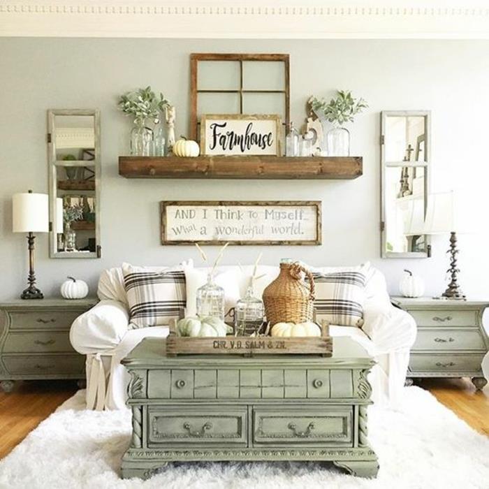 elegantna podeželska dnevna soba, vintage pastelno zelena mizica, stena v pastelnih barvah, beli kavč in črno -bele blazine, pravokotna ogledala, lesene police, demijohn, okrasne lesene plošče