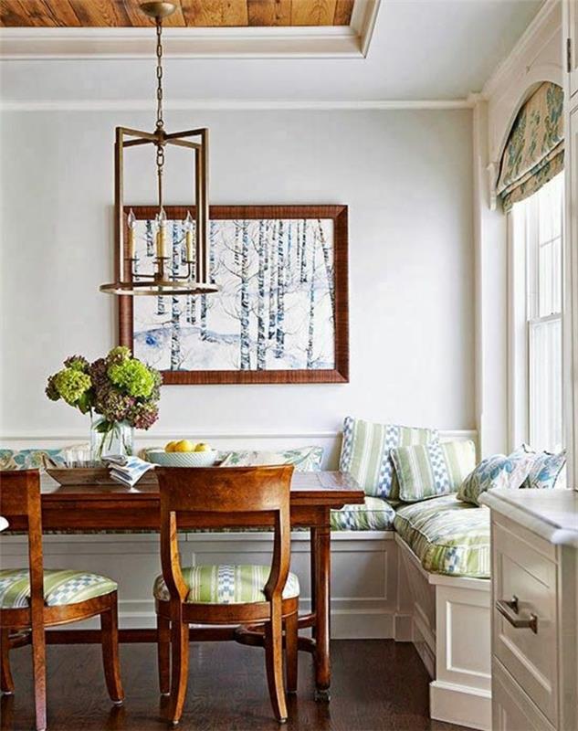 Ideja za dekor podeželske elegantne dnevne sobe, kmečka lesena miza in stoli, kotni kavč, zelene in modre blazine, vintage viseča svetilka, dekorativno slikanje, nordijski gozd