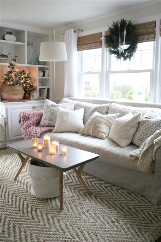 skandinaviškos ir tradicinės šventinės dvasios kupinas atostogų dekoras su minkšta sofa, papuošta pagalvėlėmis, kavos staliuko dekoracija žvakėmis ir gražia eglute krepšyje