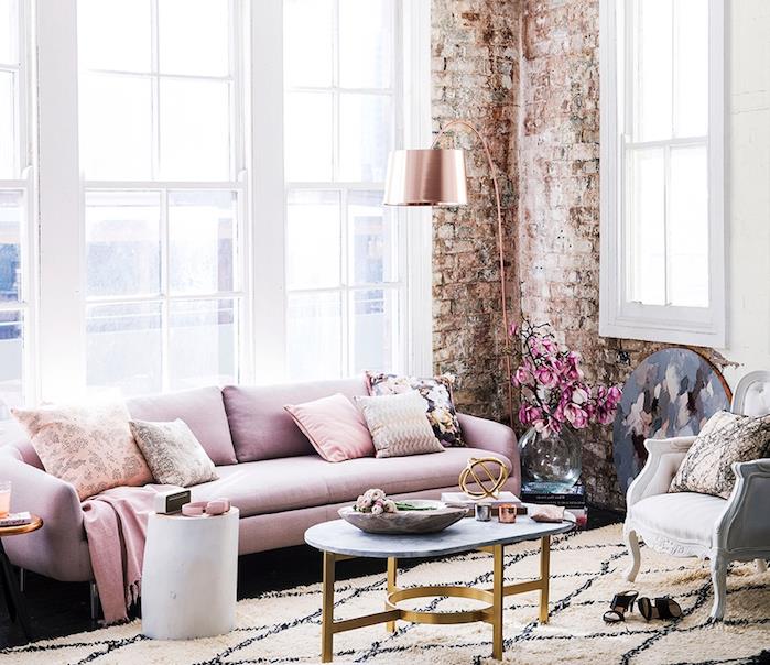 primer deko v industrijskem slogu v ženski dnevni sobi z rožnatim kavčem, mizo iz marmorja in medenine, črno -belo preprogo, opečnato steno, svetilko iz rožnatega zlata