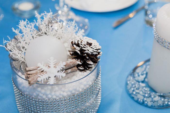Mavi bir masa örtüsü üzerinde küçük sahte kar taneleri ve çam kozalakları ile Yılbaşı masa dekorasyonu