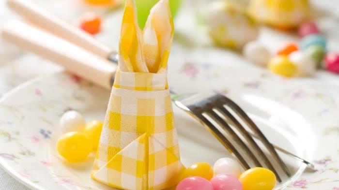 kako zložiti papirnate prtičke za okrasitev velikonočne mize, rumeno -beli karirani prtiček zložen v velikonočnega zajca