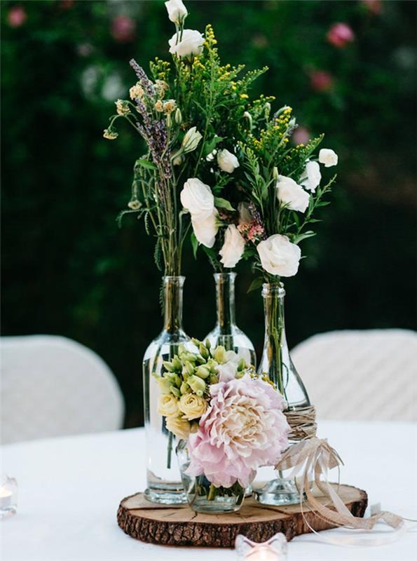 vestuvių stalo dekoras, kaimiškas stilius, medinis rąstas, vyno buteliai, apvynioti odine virvele, gėlių puokštė