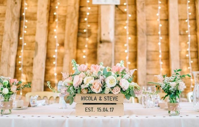 vestuvių stalo dekoravimo pavyzdys, balta staltiesė, gėlių medinė dėžė, ką daryti su stikliniais indeliais, vazos, dekoruotos džiuto juostomis ir juostele, šviesios girliandos
