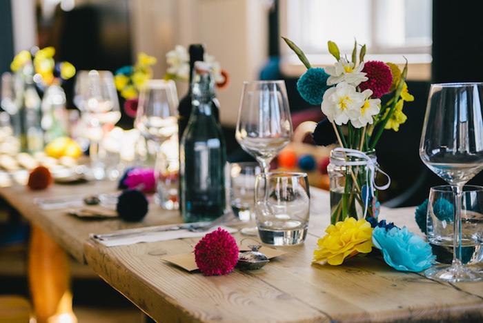 okrasitev poročne mize v stilu country chic iz surovega lesa, pisani pomponi, rože iz blaga, stekleni kozarci s cvetjem v njem