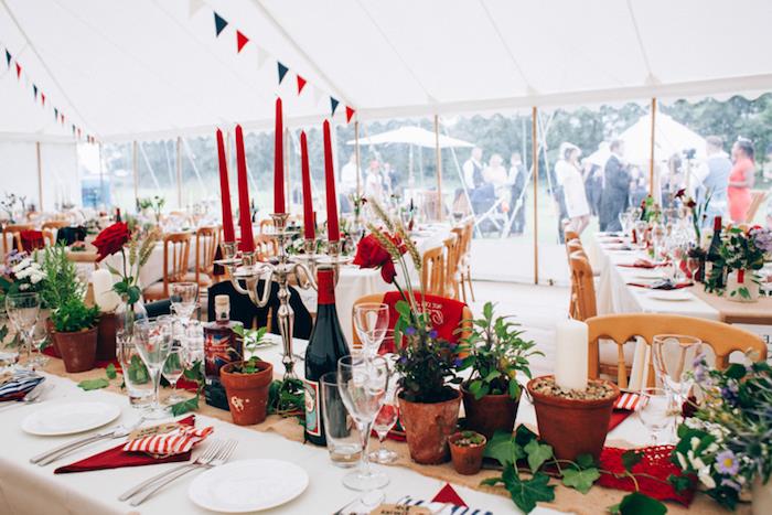 rdeča dekoracija poročne mize, svečnik z rdečimi svečami, tekač za mizo iz jute, cvetlični lonci, bršljan, venec zastavic