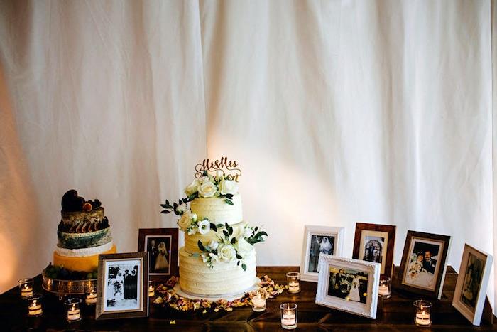 dekor za poročno mizo, torta, obdana z okraski, svečami, cvetnimi listi, par okvirji za fotografije, predniki