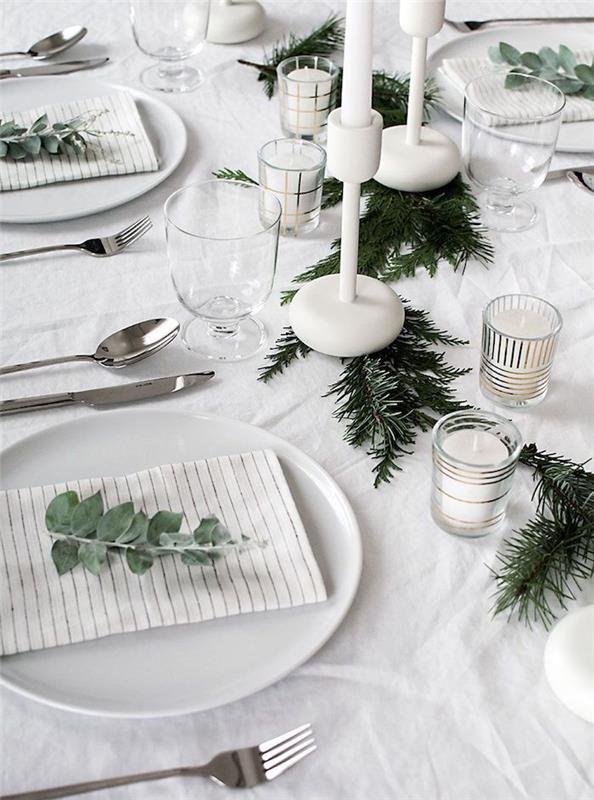 beyaz bir masa dekorasyonunu yenilemek için çam dalları, beyaz şamdanlar, gri çatal bıçak takımı, okaliptüs yeri kutusu işareti, İskandinav Noel masa dekorasyon fikri