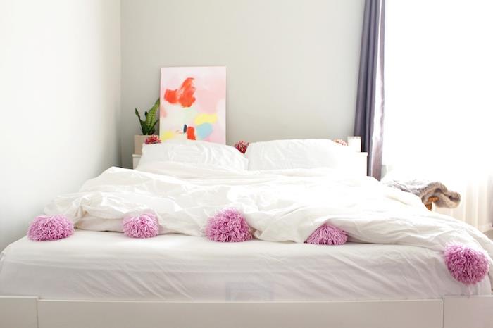 belo posteljnino, okrašeno s pomponi in originalnim vzglavjem v abstraktni umetniški dekorativni sliki za posteljo