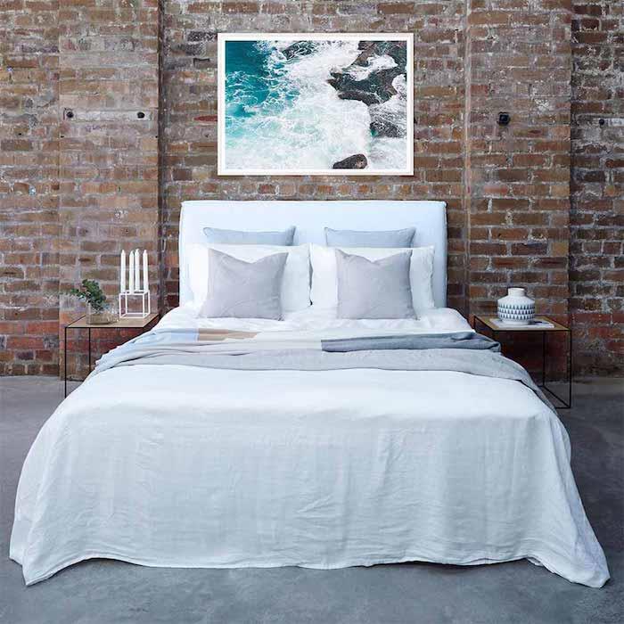 model vzglavja za fotookvir ob morju z belo in sivo posteljnino, opečna stena za posteljo, deko v industrijskem slogu