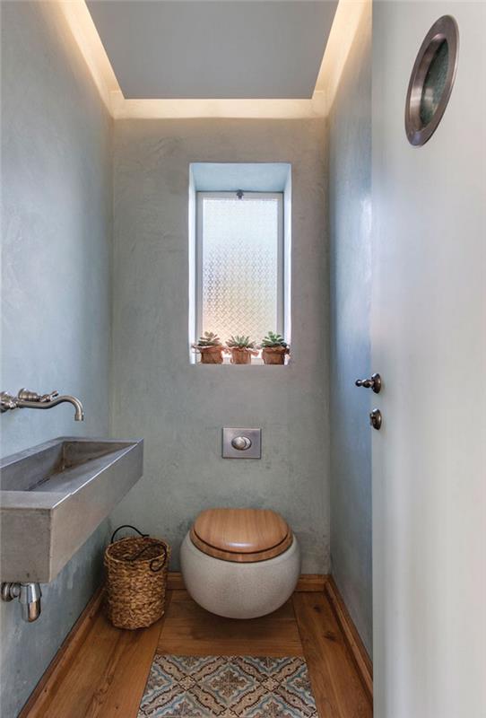 Dekoracija stranišča s sivimi stenami, okroglim visečim wc -jem in izvirnim kovinskim umivalnikom v industrijskem slogu
