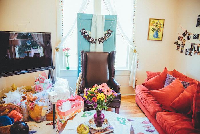draugų temos vakarėlio dekoras, rudos odos fotelis, raudona sofa, šviesaus medžio parketas, gėlių puokštė ant kavos stalo