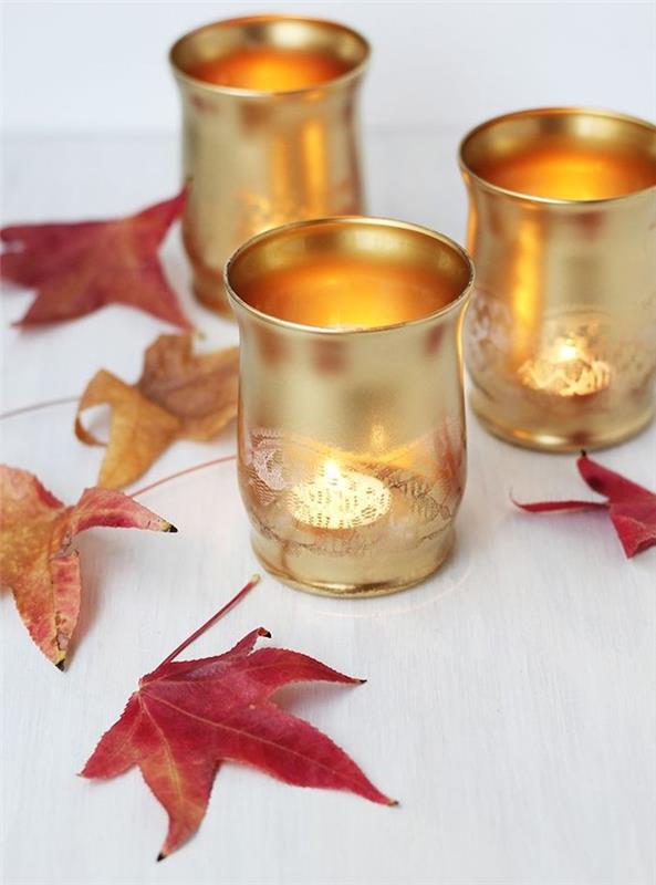 stekleni svečniki, prebarvani z zlato barvo z učinkom čipke na mizi, okrašeni z odpadlim listjem, preprosta jesenska dekoracija mize